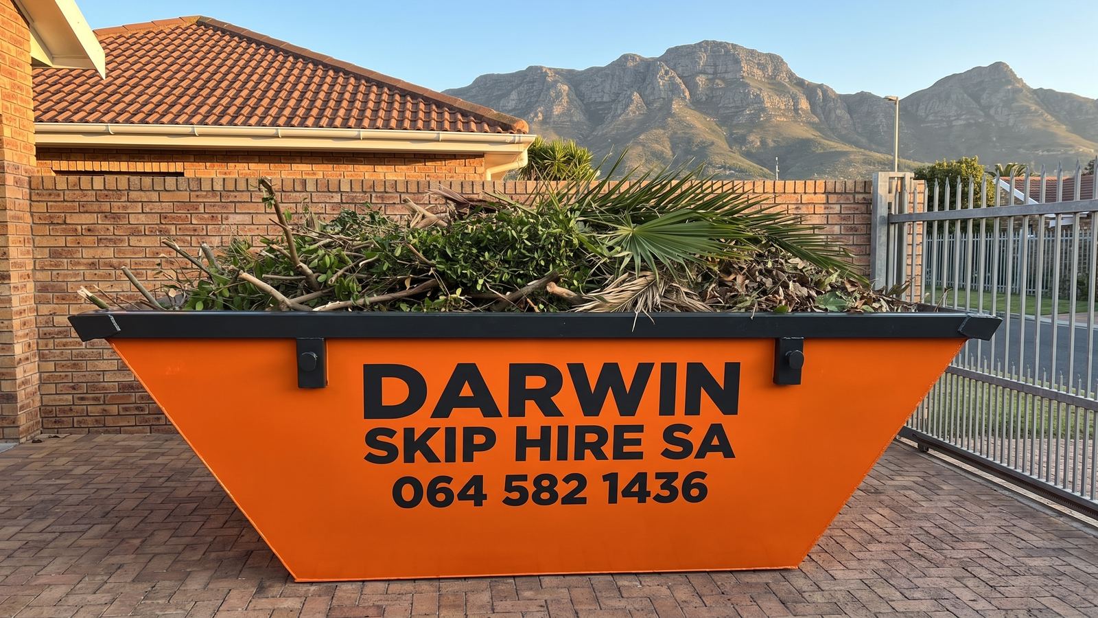 Orange Darwin Skip Hire SA skip full of branches and palm fronds with mountains behind.